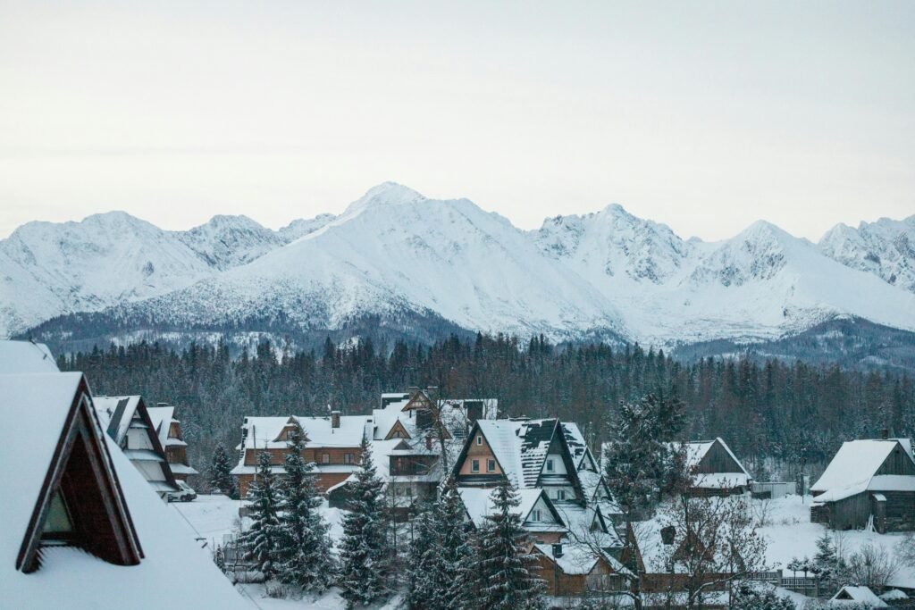 10 itens essenciais para sua mala de inverno no leste europeu: não viaje sem estes! Charming winter scene in a Polish village with snowy rooftops and mountain backdrop.