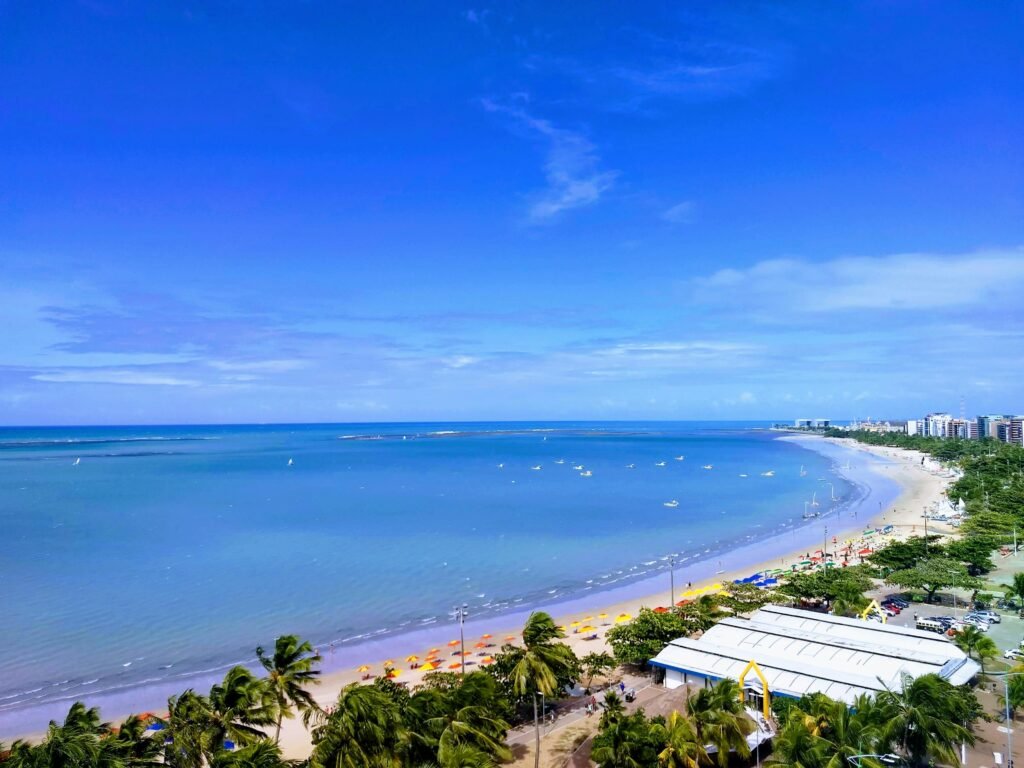 4 Itens indispensáveis para curtir as praias de Maceió A picturesque beachfront city with palm trees and clear blue skies, perfect for relaxation.