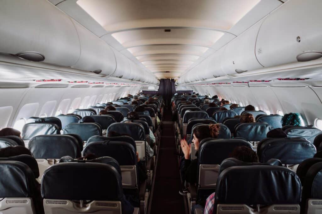 5 dicas para suportar um voo de classe econômica sem perrengues A view of passengers seated inside a commercial airplane cabin during flight.
