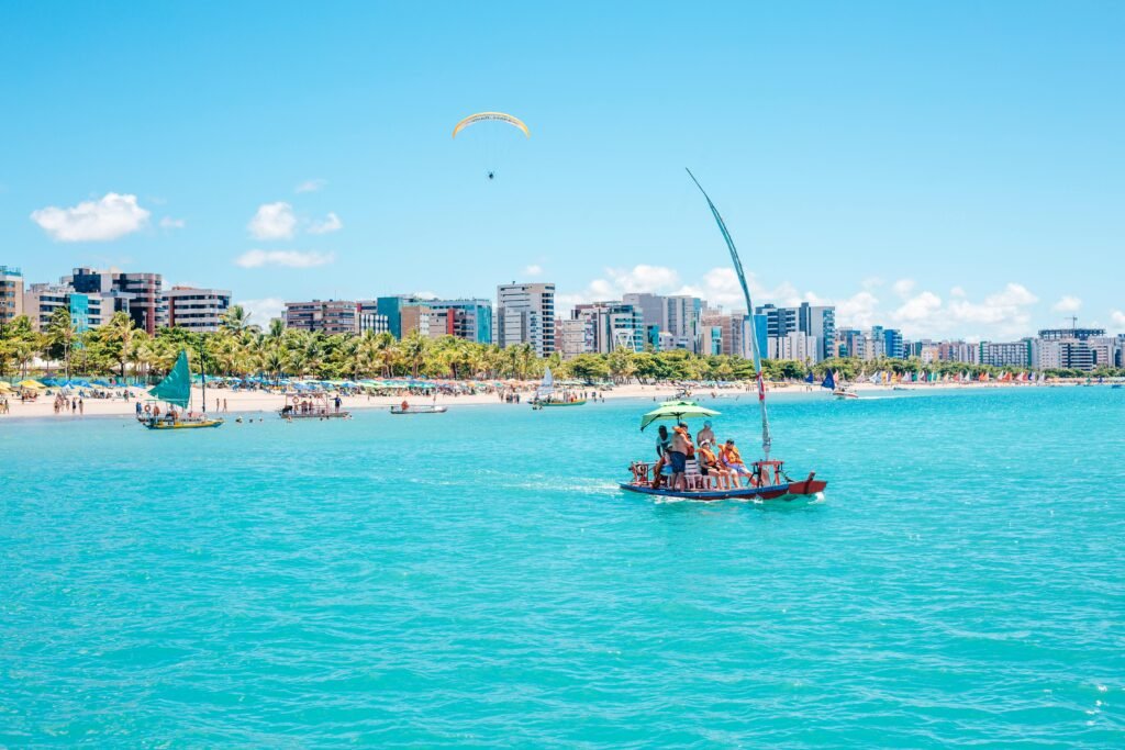 4 Itens indispensáveis para curtir as praias de Maceió Scenic view of a boat ride along the turquoise waters of Maceió, Brazil with a city skyline backdrop.