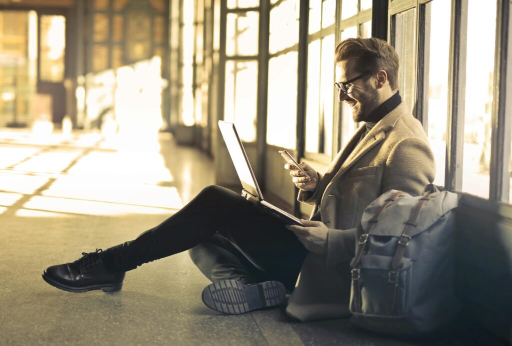 4 Itens essenciais para viajantes se distraírem no aeroporto Man sitting with a laptop and smartphone, representing digital nomad lifestyle and remote work.