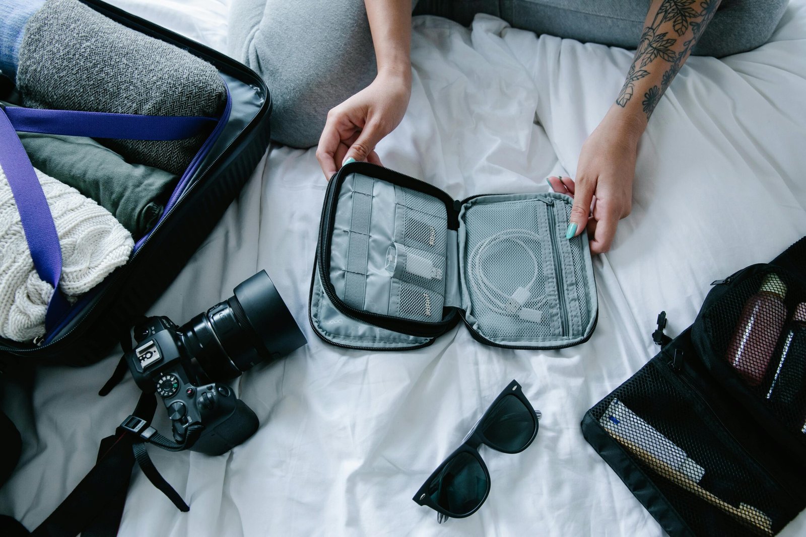 Home Traveler organizing essentials including a camera and packing cubes on a hotel bed.