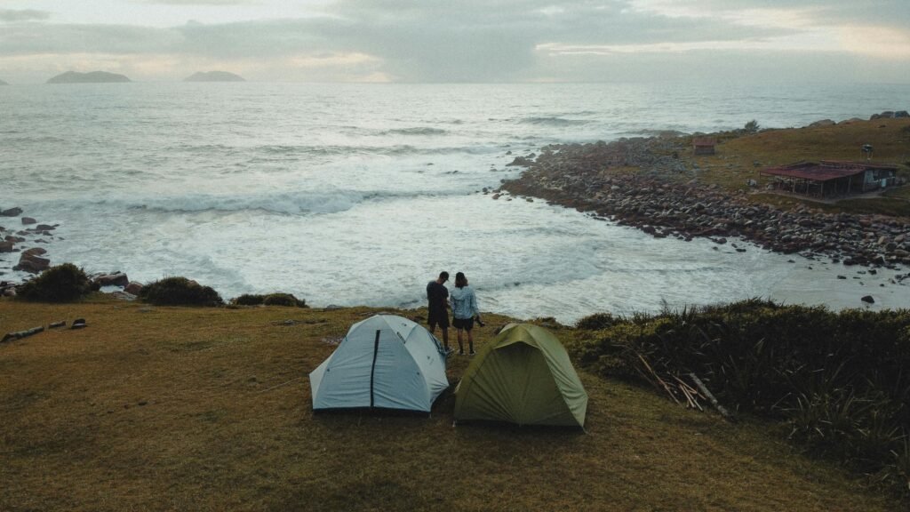 Checklist de acampamento para iniciantes: o que levar Two tents and a couple enjoying a scenic coastal view in Palhoça, Brazil.
